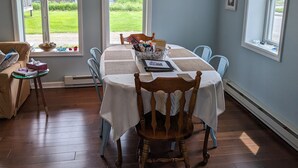 Un coin repas avec une table dressée pour quatre personnes, entourée de chaises. Une fenêtre offre une vue sur un jardin et un bâtiment à l’extérieur.