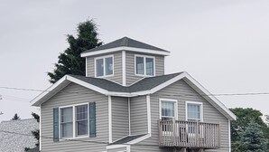 Une maison à plusieurs étages avec un balcon, une véranda dotée d’un banc et un garage.