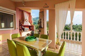 A balcony with a table and chairs, a view of greenery, and a window with curtains.