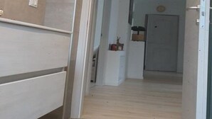 A hallway with a wooden floor, a white door at the end, and a small table with a plant. - Hidden Gem in Trentino  Authentic Alpine Stay in the Dolomites with AC (Mattarello)