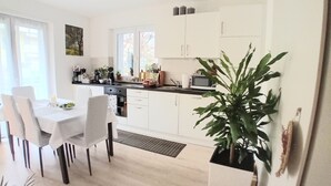 A modern kitchen with white cabinets, a dining table with chairs, and a large potted plant. - Hidden Gem in Trentino  Authentic Alpine Stay in the Dolomites with AC (Mattarello)
