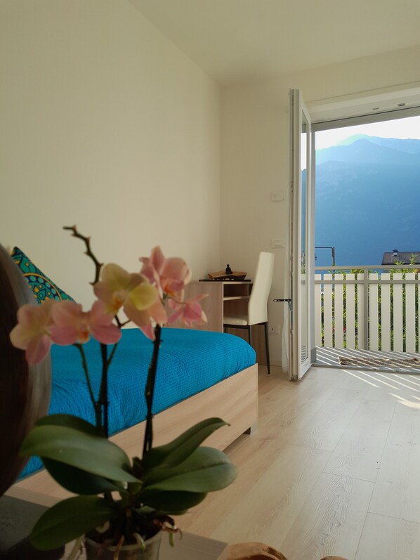 A bedroom with a bed, a desk, and a balcony with a view of the mountains.