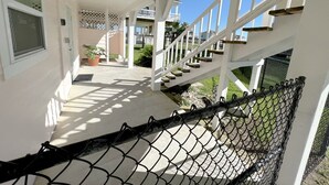 Eine überdachte Veranda mit weißer Geländer, eine Treppe, die zu einer zweiten Ebene führt, und ein Maschendrahtzaun im Vordergrund.