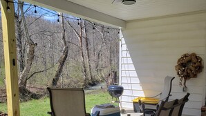 A covered patio with two chairs, a table, a cooler, and a ceiling fan. - Creekside cottage home near Red River Gorge and Natural Bridge State Park (Stanton)