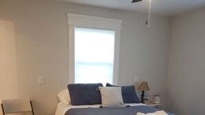 A bedroom with a bed, a ceiling fan, a window, a chair, and a nightstand with a lamp. - Creekside cottage home near Red River Gorge and Natural Bridge State Park (Stanton)