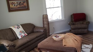 A living room with a brown leather couch, a brown ottoman, a wooden coffee table, a standing lamp, a window with a view, and a red chair. - Creekside cottage home near Red River Gorge and Natural Bridge State Park (Stanton)