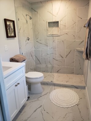 A bathroom with a toilet, a sink, and a shower area with marble tiles. - Creekside cottage home near Red River Gorge and Natural Bridge State Park (Stanton)