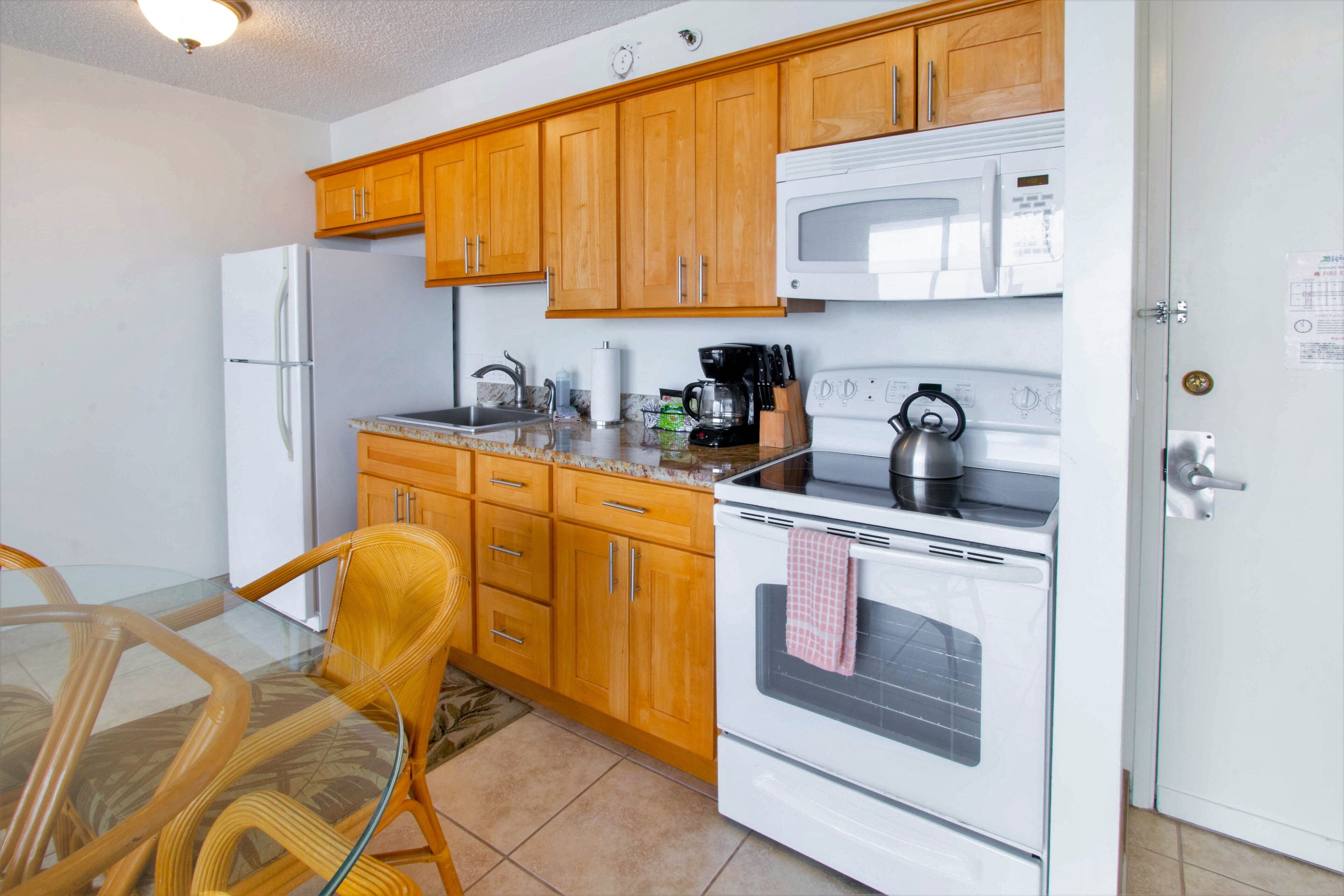 A kitchen with wooden cabinets, a refrigerator, a microwave, a stove, and a glass dining table with chairs.