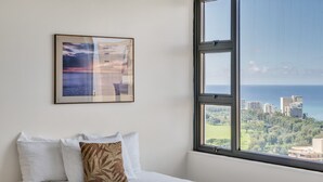 A hotel room with a bed, a large window with a city view, and a framed artwork on the wall. - Waikiki Banyan Condo With Panoramic 37th Floor Ocean Views (Honolulu)