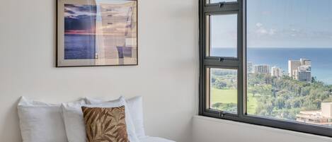 Une chambre d’hôtel avec un lit, une grande fenêtre donnant sur la ville et une œuvre d’art encadrée au mur.