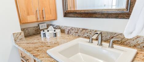 A bathroom with a granite countertop, a white sink, and wooden cabinets.