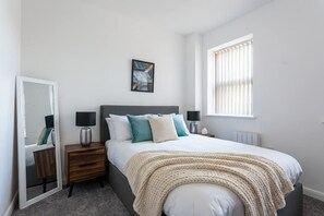 A bedroom with a bed, bedside tables, a mirror, a window, and a radiator. - Modern 2 Bedroom Bolton Apartment with WiFi (Bolton)