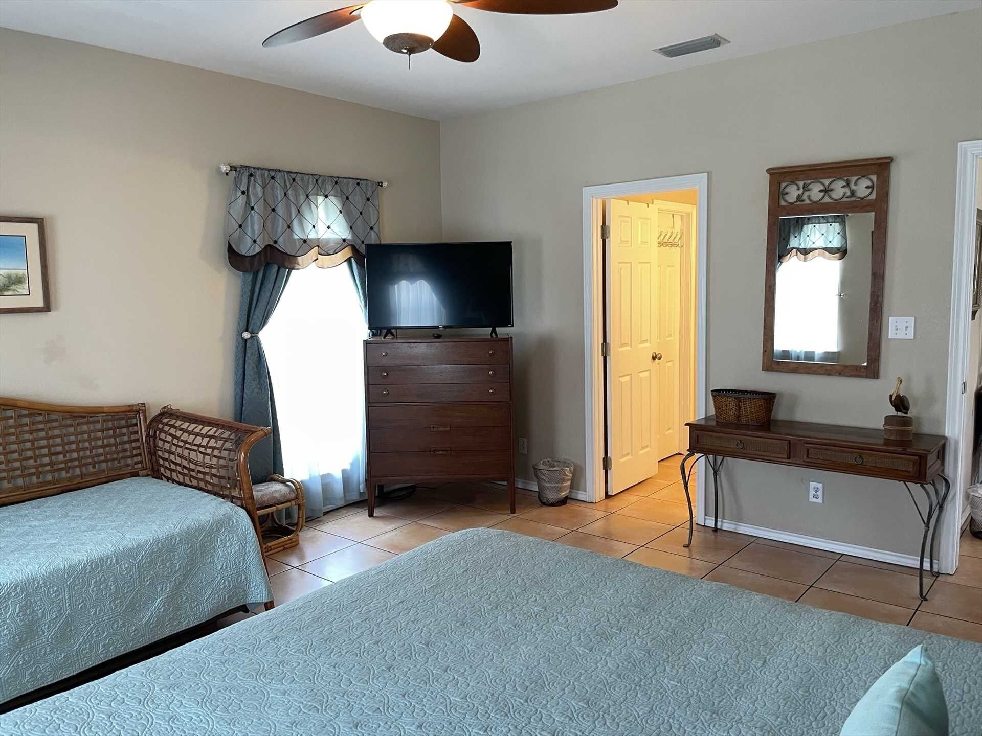 A bedroom with two beds, a dresser, a television, and a door leading to another room.