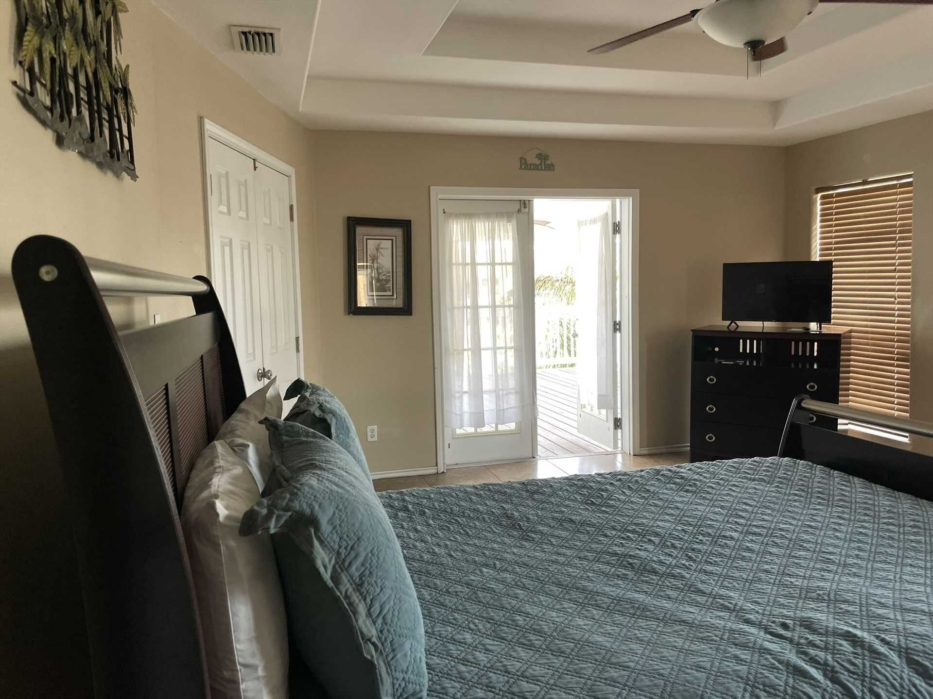 Quarto com cama, penteadeira, televisão e porta que dá para uma varanda.