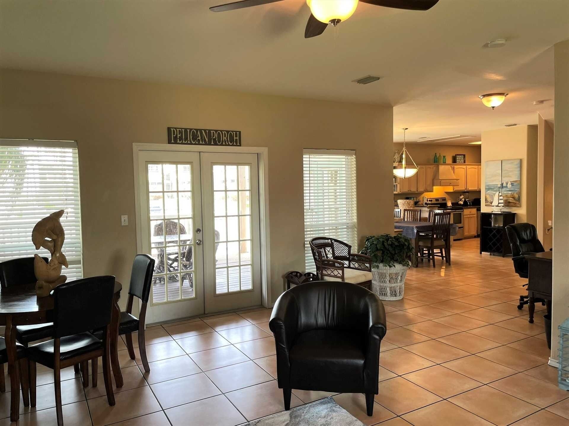 A spacious living room with a dining area, a kitchen in the background, and a door labeled "PELICAN PORCH".