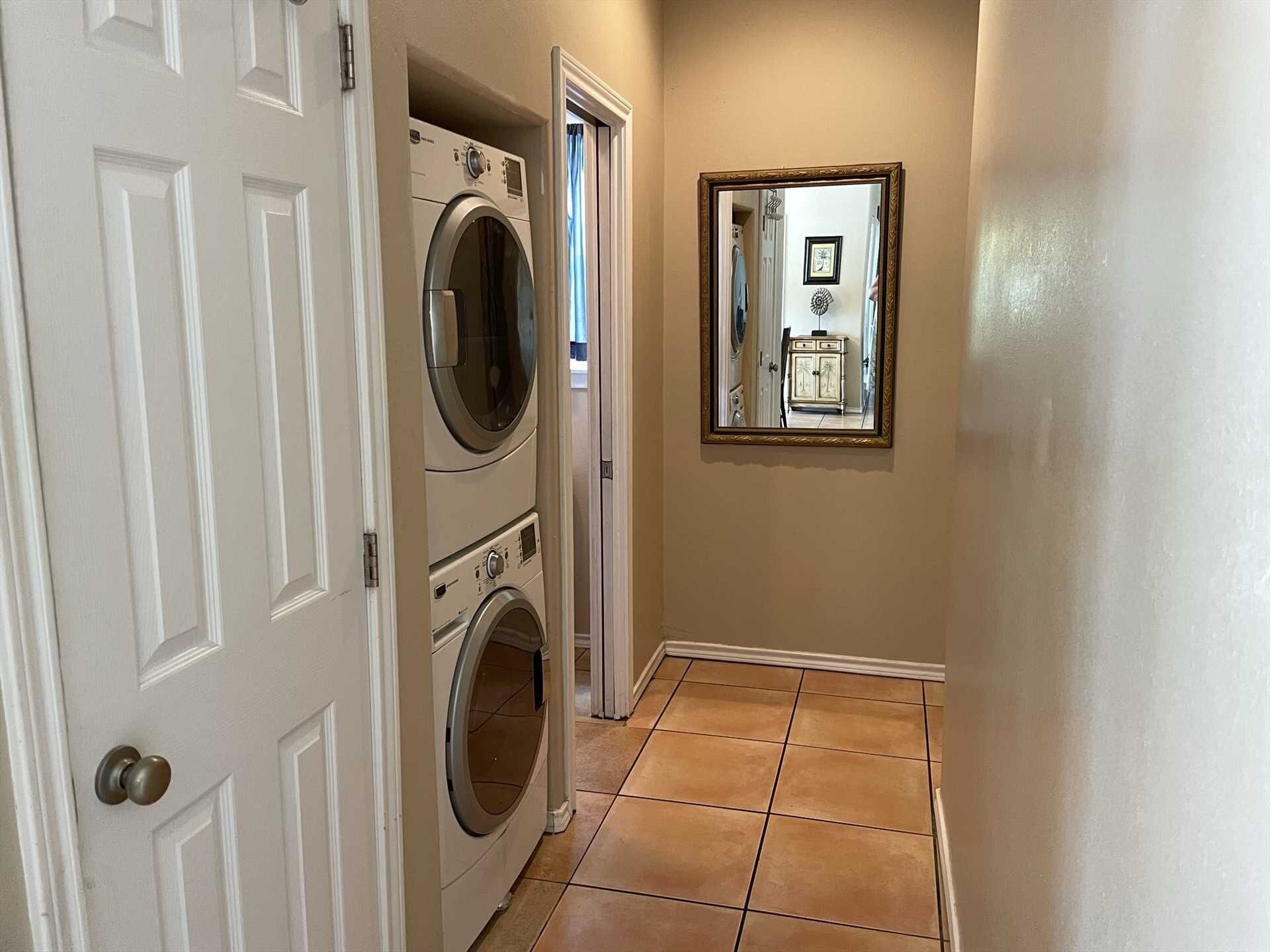 A hallway with a washing machine, a door, and a mirror reflecting a cabinet.