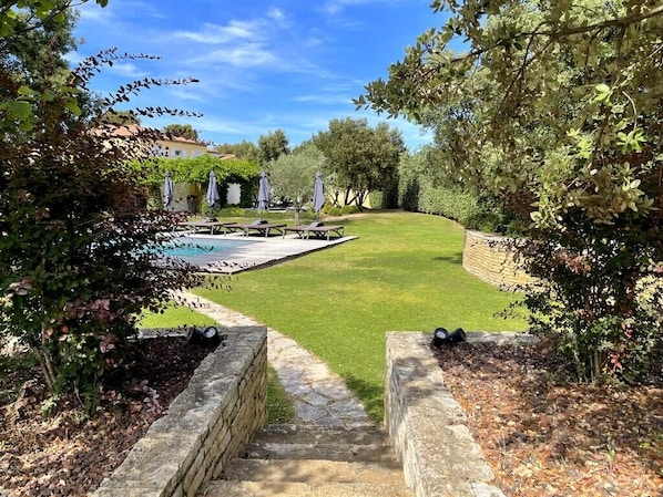 A pathway leading to a pool area with picnic tables and umbrellas.
