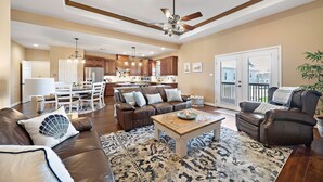 A spacious living room with a brown leather sofa, a coffee table, and a patterned rug. A dining area with a white table and chairs is visible in the background. - Copper Top | Moments from Beach (Galveston)