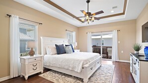 A bedroom with a bed, nightstand, dresser, ceiling fan, and a view to the outside. - Copper Top | Moments from Beach (Galveston)