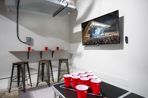 A room with a bar area, stools, a television mounted on the wall, and a table with red cups. - Nashville getaway: themed house with garage game room, sleeps 12 (Nashville)