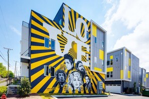 Ein modernes Gebäude mit einer auffälligen gelb-schwarzen Fassade, das ein großes Wandgemälde mit vielen Gesichtern zeigt und das Wort 'LOVE' großflächig präsentiert.