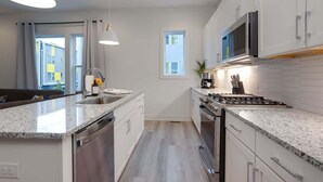 Een moderne keuken met witte kastjes, granieten aanrecht en een roestvrijstalen fornuis en magnetron.