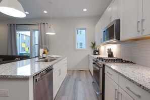 A modern kitchen with white cabinets, granite countertops, a stainless steel stove, and a microwave. - music city themed home with garage game room, sleeps 12 in east nashville (Nashville)