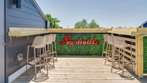 Een buiten zitgedeelte met twee rieten stoelen en een houten tafel, een groene muur met 'Nashville' erop, en een heldere lucht.