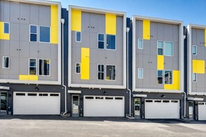 A modern multi-story building with a grey facade, yellow accents, and white garage doors.