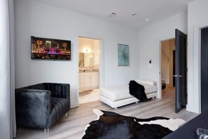 Una sala de estar moderna con un sofá de cuero negro, un sofá blanco y un tapiz de cuero de vaca. En la pared hay un cuadro de un paisaje urbano.