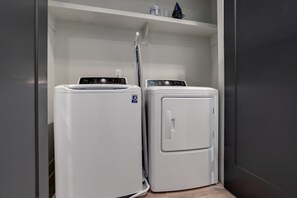 Une buanderie équipée de deux machines à laver à chargement frontal superposées et d’une étagère placée au-dessus.