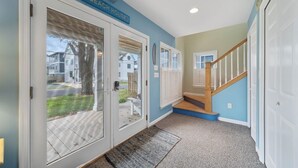 A hallway with a 'Beach House' sign, a wooden staircase, and a view of houses through glass doors. - Located on prime street in Dewey Beach walking to everything with brand new POOL (Dewey Beach)