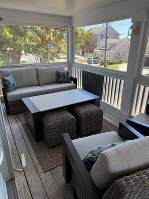 Een overdekte veranda met een bank, poefs en een tafel.