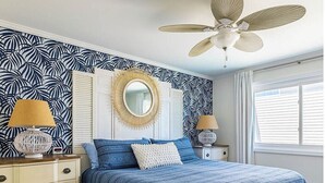 Una camera da letto con un letto, comodini, una ventola a soffitto e una finestra con persiane.