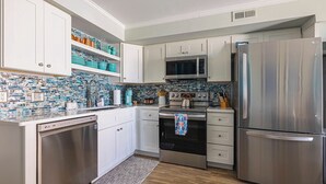 Una cucina moderna con mobili bianchi, elettrodomestici in acciaio inossidabile e una parete di fondo rivestita di piastrelle blu e bianche.