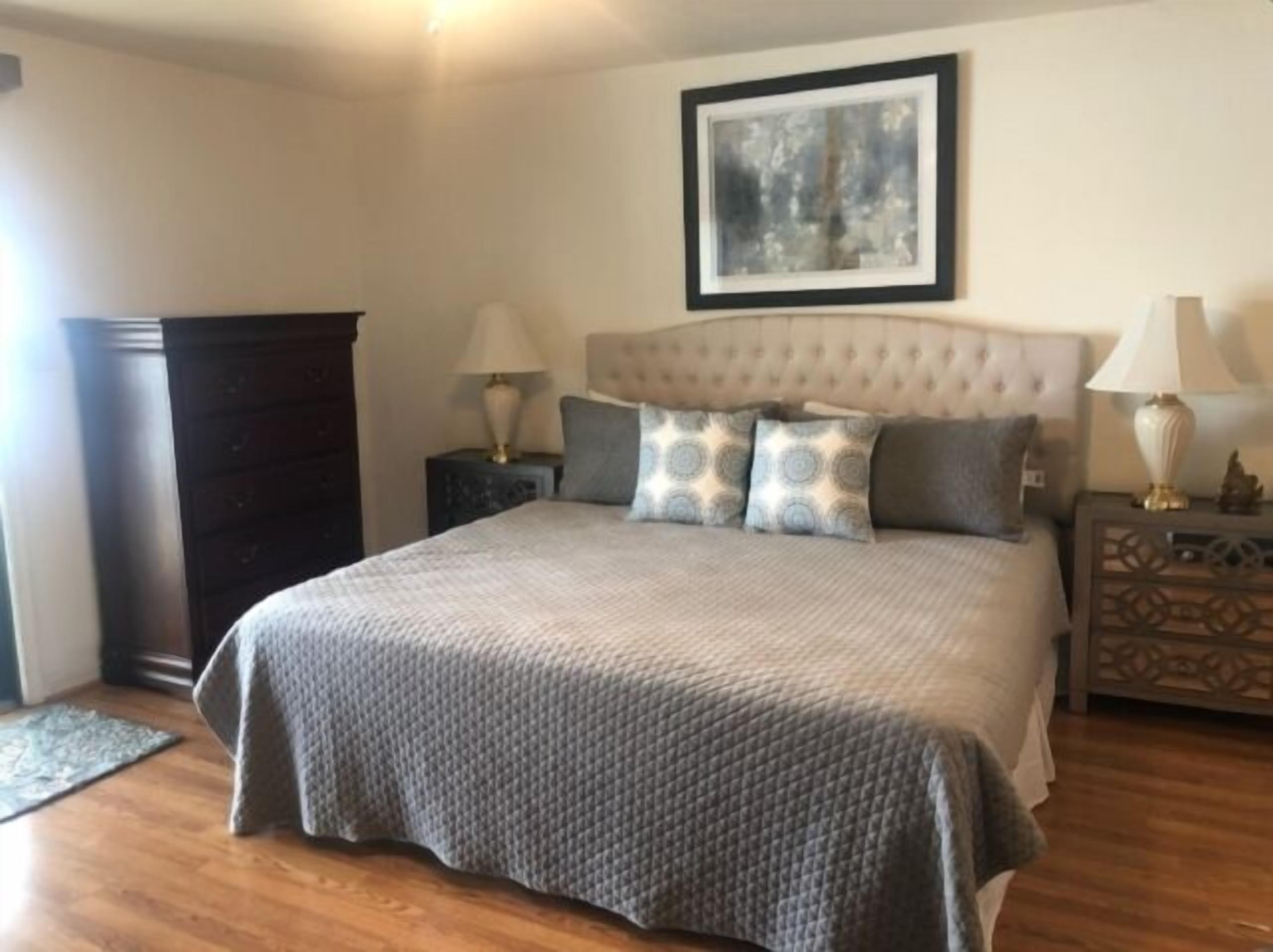 Une chambre à coucher avec un grand lit, deux tables de chevet, une commode et une œuvre d’art encadrée accrochée au mur.