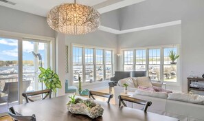 A spacious living room with large windows, a dining area, and a piano. - Marina View Condo w/Pool Access (Spring Lake)