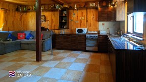 Une cuisine compacte avec des meubles en bois, un four à micro-ondes, une cuisinière et un évier. Le salon est équipé d’un canapé avec des coussins.