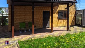 Un bâtiment d’un seul étage, doté d’un toit en tuiles, d’une façade en briques et d’un patio couvert avec deux chaises vertes.