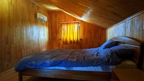 Une pièce aux murs lambrissés, avec un lit, une fenêtre avec des rideaux et un appareil de climatisation.