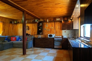 Eine kompakte Küche mit Holzausstattung, einer Mikrowelle, einem Herd und einem Spülbecken. Im Wohnbereich befindet sich eine Couch mit Kissen.