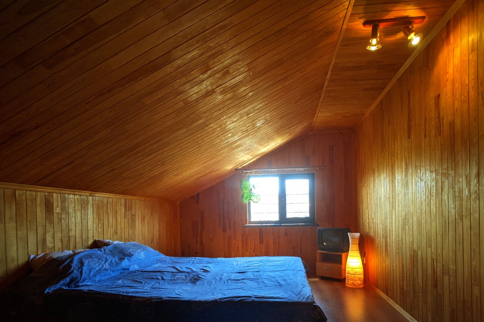 Una habitación de madera con una cama, un ventanal con vistas y un altavoz en la pared.
