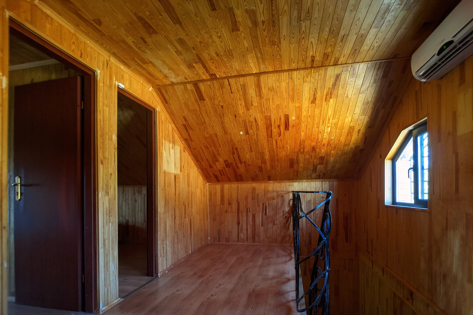 Interior de madeira com teto inclinado, janela e porta.