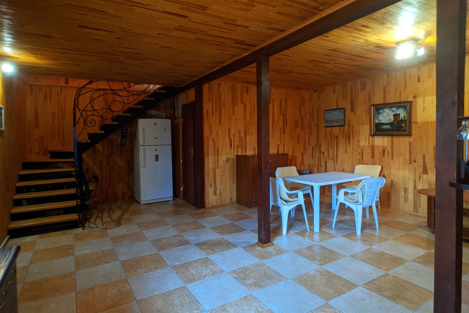 Un interior de madera con piso a cuadros, una mesa de comedor con sillas, un refrigerador y una escalera.