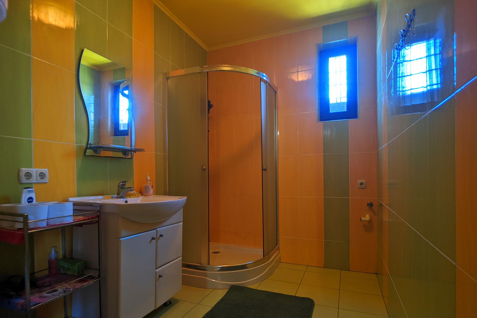 A bathroom with a curved glass shower, a sink, and a mirror.