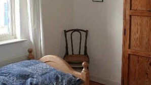 Ein Schlafzimmer mit einem hölzernen Bett, einem Sessel, einem Kleiderschrank und einem Fenster mit Vorhängen.