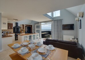 Enjoy meals in this spacious living area with a dining set and modern kitchen in the background.