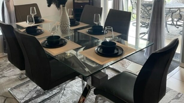 A dining area with a glass table, black chairs, and a chandelier. - 4 Miles from Disney Hollywood Themed Home (Kissimmee)