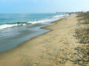 Une plage avec une jetée en arrière-plan, un rivage sablonneux et des empreintes de pas.