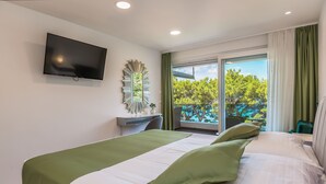 Quarto de hotel com uma cama, televisão fixada na parede, escrivaninha e janela com vista para árvores.